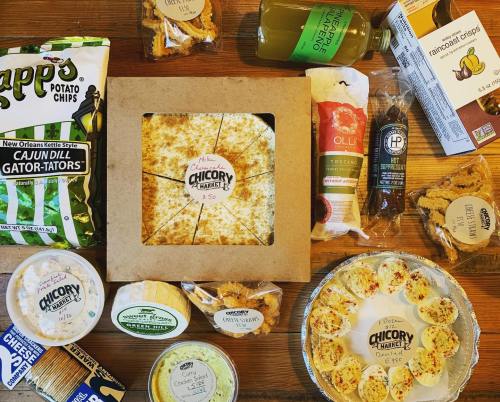 A variety of snacks including chips, cheeses, and dips arranged on a wooden surface, featuring a cheese wheel at the center.