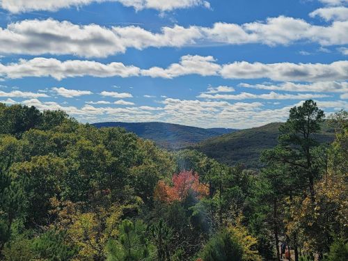 A scenic view of rolling hills and colorful trees under a blue sky with fluffy clouds.