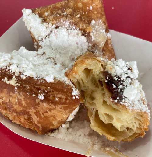 A close-up of flaky pastries dusted with powdered sugar, with one partially broken open to reveal its soft interior.