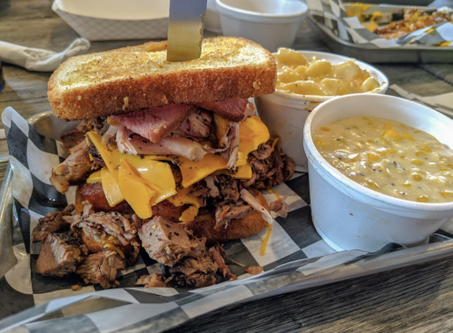 A hearty sandwich stacked with meats and cheese, served with sides of macaroni and cheese and corn chowder.