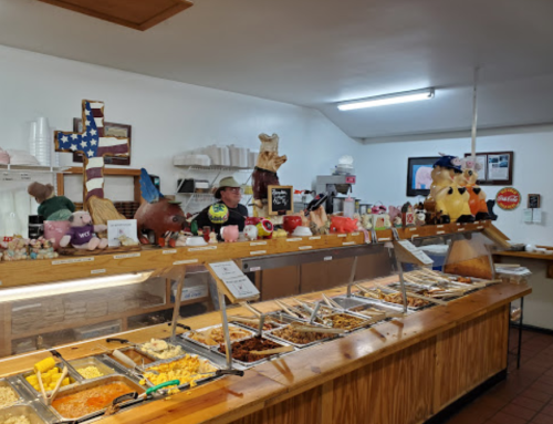 A buffet with various dishes, a smiling server, and decorative figures on the counter in a cozy dining space.