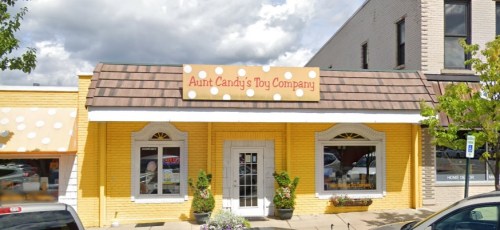 Bright yellow storefront of Aunt Candy's Toy Company, featuring a sign with polka dots and large windows.
