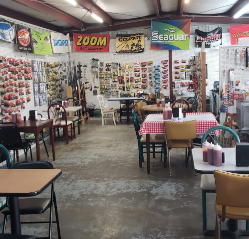 A fishing supply store with tables, chairs, and walls lined with fishing gear and bait company banners.