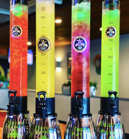 Four colorful drink towers filled with vibrant beverages, each labeled with measurement markings, on a bar counter.