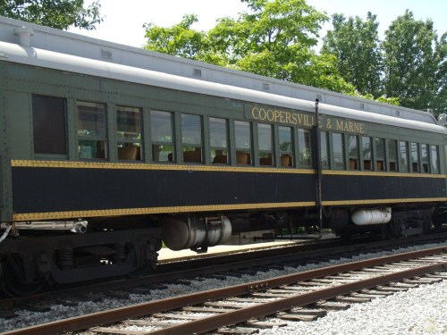 A vintage train car labeled "Coopersville & Marne" parked on a railway surrounded by greenery.