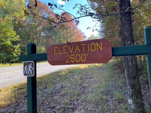 Sign indicating an elevation of 2500 feet, with a hiking symbol nearby, surrounded by trees and autumn foliage.