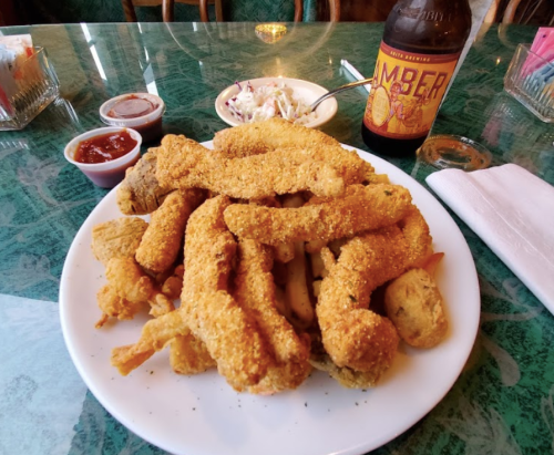 A plate of golden fried fish and chicken, served with dipping sauces and a bottle of amber beer on a green table.