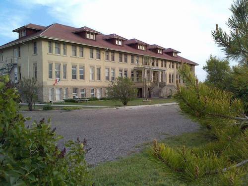 Historic building with a red roof, surrounded by greenery and a gravel path, under a clear sky.