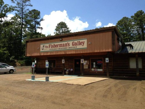A rustic wooden building with a sign reading "The Fisherman's Galley," featuring a seafood buffet, surrounded by trees.