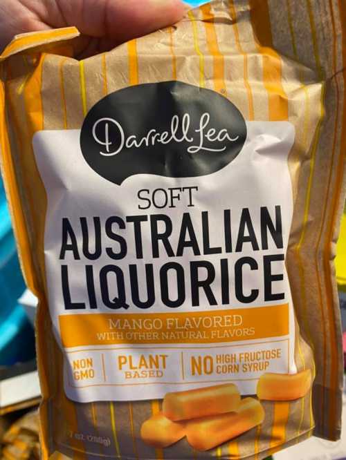 A hand holding a bag of Darrell Lea soft Australian liquorice, mango flavored, with a striped yellow and white design.