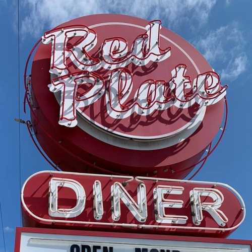 A bright red diner sign with the words "Red Plate Diner" in bold white letters against a blue sky.