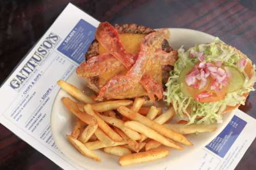 A cheeseburger topped with bacon, lettuce, tomato, and onions, served with a side of French fries on a menu backdrop.