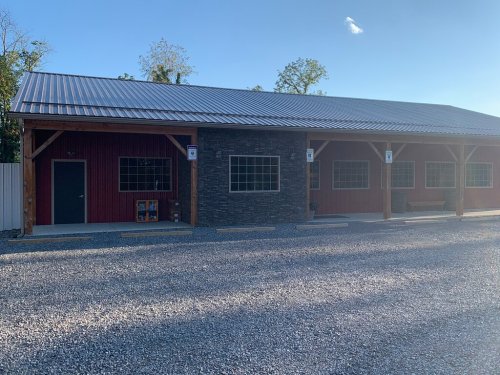 A red building with a stone accent wall, featuring large windows and a gravel parking area in front.