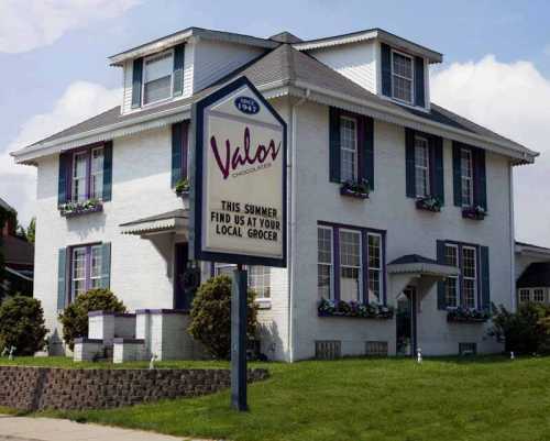 A charming white house with purple accents and a sign for Valos Grocers, inviting customers to visit their local store.