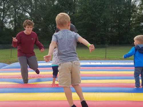 Children jumping and playing on a colorful inflatable bounce house in a grassy outdoor setting.