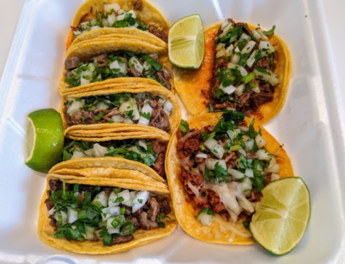 A tray of tacos topped with onions and cilantro, served with lime wedges.