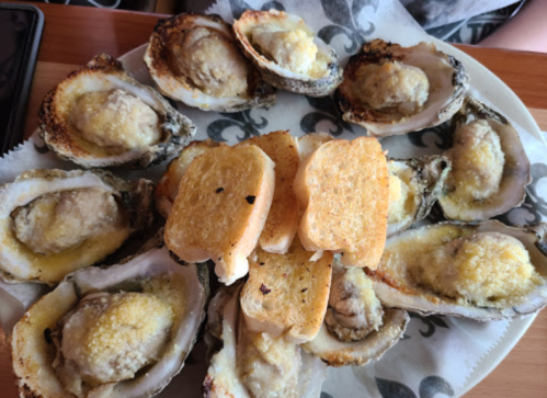 A plate of baked oysters topped with cheese, accompanied by toasted bread slices.