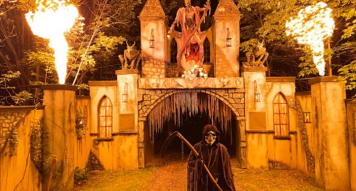 A spooky haunted house entrance with flames, a grim reaper figure, and eerie decorations in a dark forest setting.