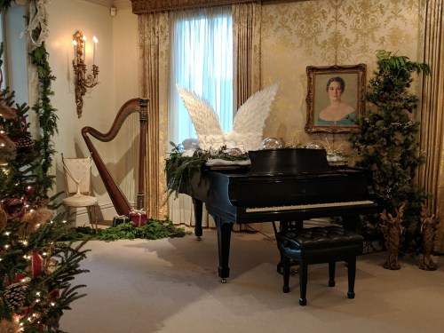A decorated room featuring a grand piano, a harp, and a portrait, with festive greenery and holiday decor.