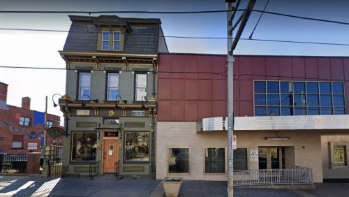 A historic building with a green facade next to a modern red and beige structure on a city street.
