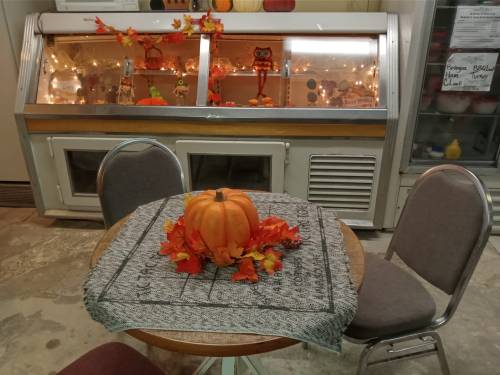 A cozy table with a pumpkin and autumn leaves, set in a room with a display case decorated for fall.