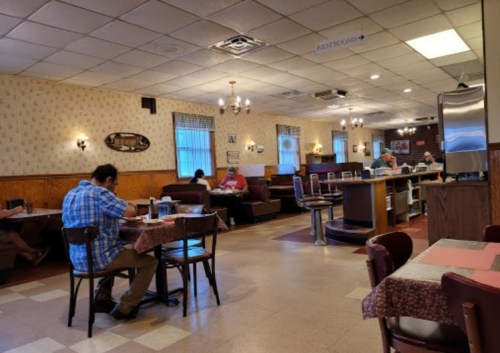 A cozy diner interior with booths and tables, patrons eating, and a counter in the background. Warm, inviting atmosphere.
