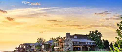 A scenic view of a large wooden lodge at sunset, surrounded by trees and a colorful sky.