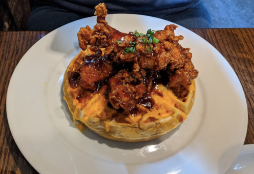 A plate featuring a waffle topped with crispy fried chicken and drizzled with sauce, garnished with green onions.