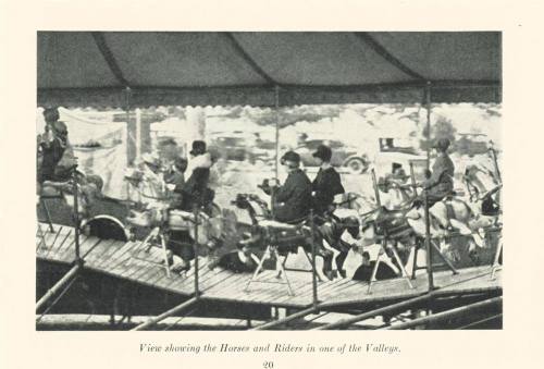 Black and white image of a carousel with riders on horses, under a tent, capturing a nostalgic amusement park scene.