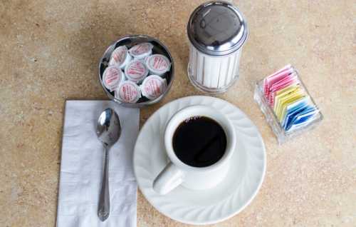 A cup of black coffee on a plate, with creamers, sugar, and a spoon on a textured surface.