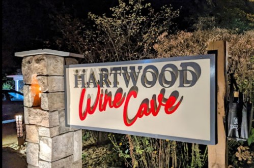 Sign for Hartwood Wine Cave, featuring illuminated letters against a stone backdrop.