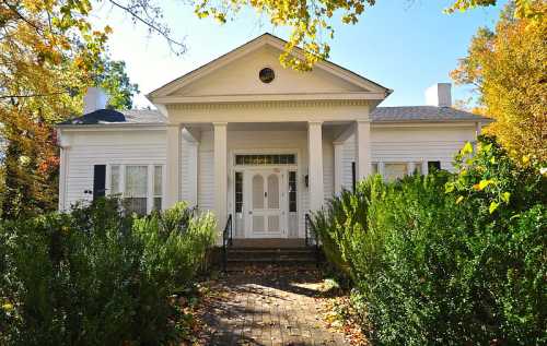 A charming white house with a front porch, surrounded by lush greenery and autumn foliage.