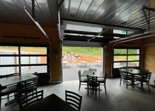 Interior of a modern space with black tables and chairs, featuring large garage doors open to an outdoor area.