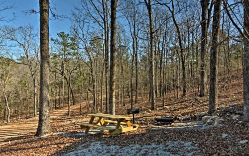 A picnic table sits in a wooded area with bare trees and fallen leaves, under a clear blue sky.
