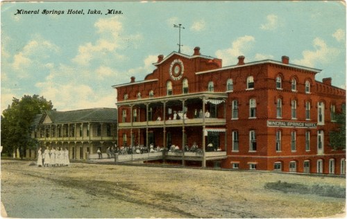 Historic Mineral Springs Hotel in Iuka, Mississippi, featuring a large porch and guests enjoying the outdoor space.