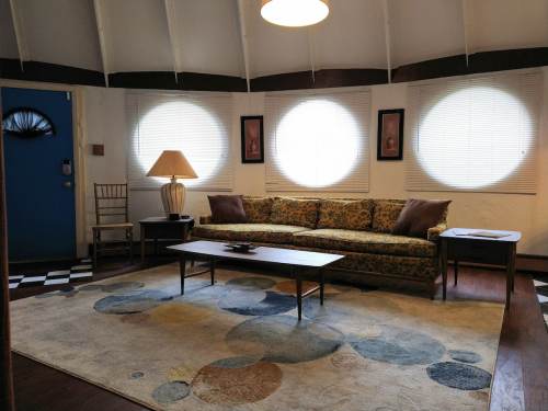 Cozy living room with a patterned sofa, round windows, a lamp, and a coffee table on a colorful rug.
