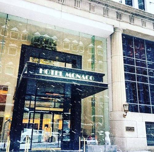 Entrance of Hotel Monaco with a glass facade, featuring snowflakes falling in front of the building.