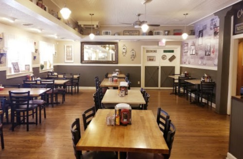 A cozy restaurant interior with wooden tables, black chairs, and vintage decor on the walls.