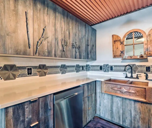 Modern kitchen with wooden cabinets, geometric tile backsplash, and a unique copper sink. Warm, rustic design elements.