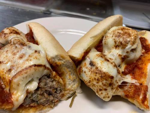 Two sandwich halves filled with meat, marinara sauce, and melted cheese, served on a white plate.