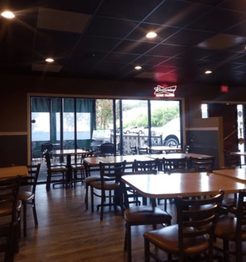 Interior of a restaurant with empty tables and a large window showing an outdoor area. Soft lighting and casual decor.
