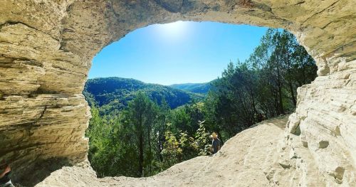 A scenic view from a rock formation, showcasing lush green hills and a bright blue sky.