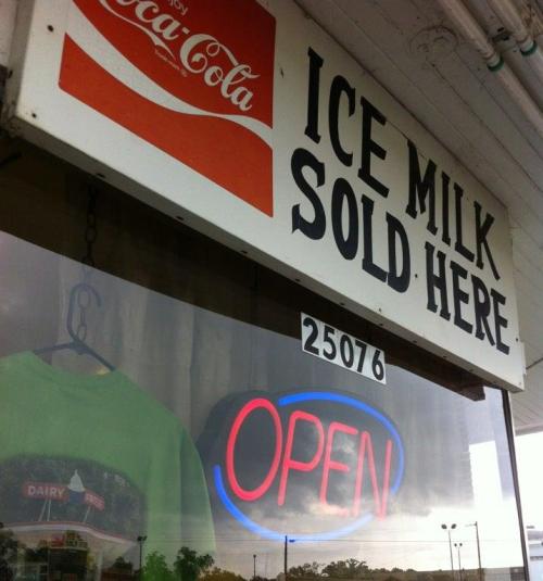 Sign outside a store reads "Ice Milk Sold Here" with an illuminated "Open" sign and a Coca-Cola logo.