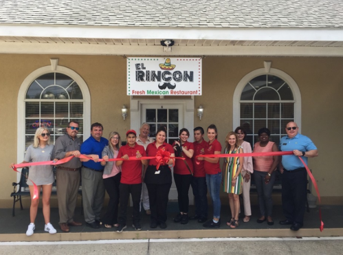 A group of people holding a ribbon in front of El Rincon, a fresh Mexican restaurant, during a grand opening ceremony.