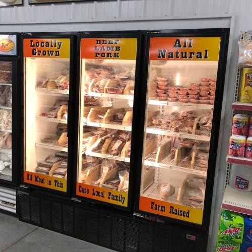 Refrigerated display case featuring locally grown, all-natural meats: beef, lamb, and pork, labeled for local family farms.
