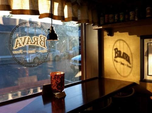 A cozy café interior with a window displaying the "Brava" logo and a candle on a wooden table, casting a warm glow.