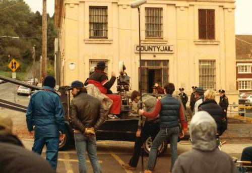 A film crew sets up outside a county jail, with cameras and equipment in a bustling scene.