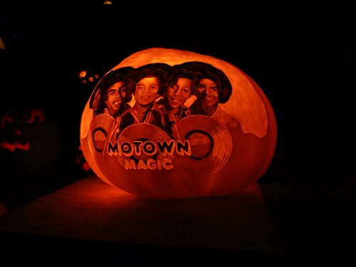 A carved pumpkin glowing orange, featuring the words "Motown Magic" and portraits of four musicians.