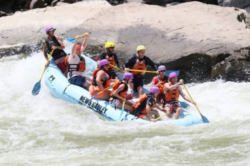 A group of people in helmets paddling a raft through whitewater rapids, enjoying an adventurous outdoor experience.