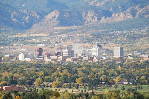 A panoramic view of a city skyline surrounded by mountains and colorful autumn foliage.